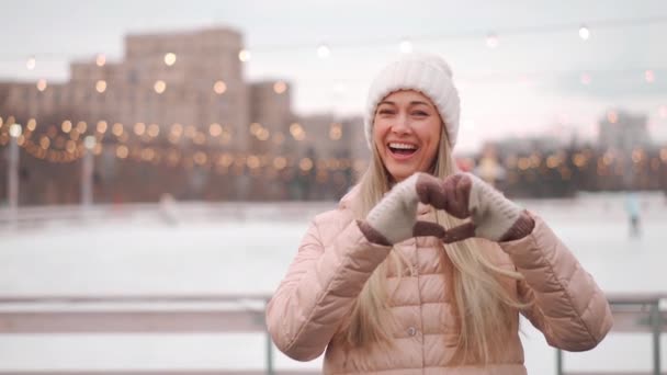 겨울. 크리스마스 연휴, 젊은 성인 여성은 스케이트장 근처 도시의 거리에서 눈이 내리는 겨울을 즐긴다. 겨울에 하얀 뜨개 질 모자를 쓴 아름다운 코카서스 암컷의 모습 — 비디오