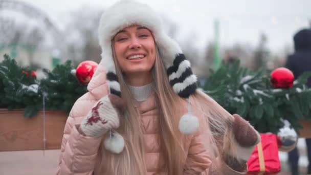 Winterzeit. Weihnachtsurlaub, junge erwachsene Frau genießt den verschneiten Winter draußen. Porträt einer schönen kaukasischen Frau mit lustigem Pelzhut. Spaß haben, Hut vor den Augen ziehen, lachen. — Stockvideo