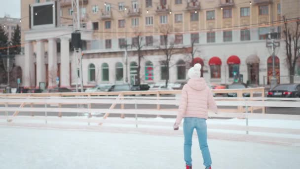 Χειμώνας. Χριστούγεννα διακοπές, γυναίκα σε πλεκτό καπέλο πατινάζ πάγο παγοδρομία ανοιχτή πόλη παγοδρόμιο στην κεντρική πλατεία της πόλης. Χειμερινή περίοδος. Καυκάσιος ενήλικος ερασιτέχνης πατινέρ πάγου — Αρχείο Βίντεο