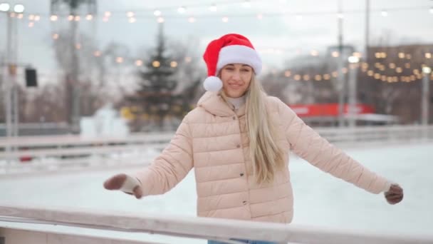 Invierno. Vacaciones de Navidad, mujer en Santa Sombrero patinaje patinaje sobre hielo de la ciudad abierta pista de hielo en la plaza central. Temporada de invierno. Caucásico adulto hembra amateur patinador de hielo — Vídeos de Stock