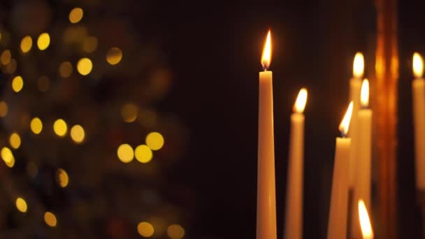Heiligabend bei Kerzenschein. Close up Kerzenfeuer mit Weihnachtsbaum Lichterkranz auf dem Hintergrund. Ruhige Szene. Feierabend gemütliche Atmosphäre zu Hause — Stockvideo