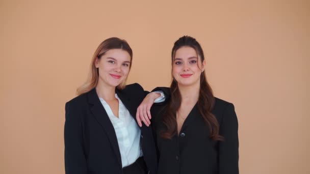 2人の若い実業家の女性が黒の正式なスーツスタジオベージュの背景に立ってカメラを着ていた。業務提携の考え方 — ストック動画