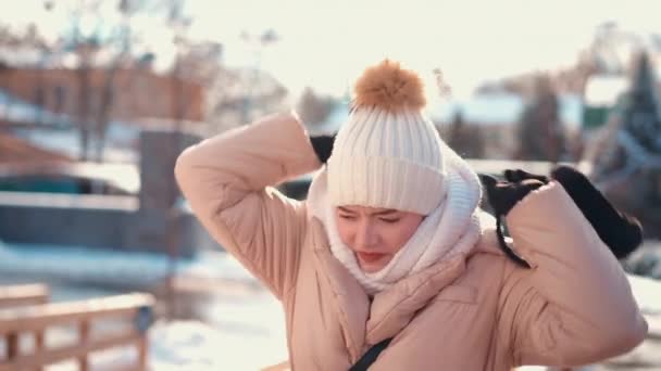 Mujer joven vestida chaqueta de invierno blanco sombrero de punto y bufanda de pie al aire libre en la calle de la ciudad de invierno — Vídeo de stock