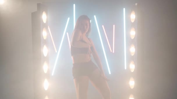 Artistic young woman dancing in backlit fog smoke indoors. Confident graceful Caucasian female dancer rehearsing modern performance with ballet movements — Stockvideo