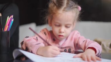 Çocuk çizimi masanın ortasında oturuyor. Beyaz kadın küçük kız renkli kalemlerle resim çiziyor. Ödev yapan kadın çocuk. 