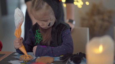 Cadılar Bayramı kurabiyelerini süsleyen küçük kız Cadılar Bayramı karnavalında boynuzlu kostüm giymiş. 