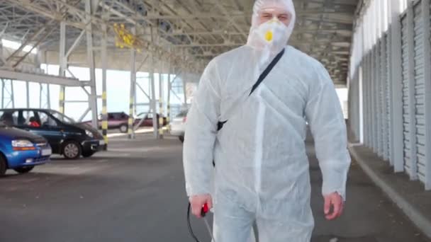 Männer in weißen Schutzanzügen gehen auf dem Parkplatz spazieren. Desinfektionsmittel gehen mit antiviralen Flüssigkeitstank suchen — Stockvideo