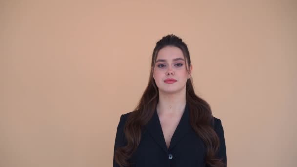 Молода біла ділова жінка 20 років одягнена в чорну куртку стоїть студії ізольовані бежевий колір фону дивиться камеру — стокове відео