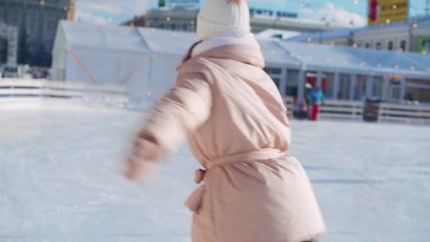 Молодая улыбающаяся женщина катается на коньках на центральной площади катка на рождественские праздники, активный зимний отдых в теплый солнечный день. Портативный эффект. Любительница кавказских фигуристок — стоковое видео