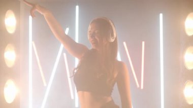 Arka planda sis dumanında dans eden sanatçı genç kadın kulaklıkları. Kendine güvenen zarif beyaz kadın dansçı modern performansı bale hareketleri ile prova ediyor.