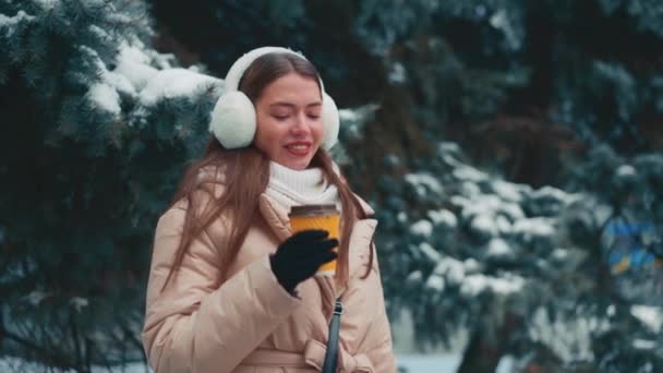 Mulher beber café ao ar livre. Dia de inverno, jovem caucasiano feminino de pé com café para ir no fundo da árvore de abeto — Vídeo de Stock