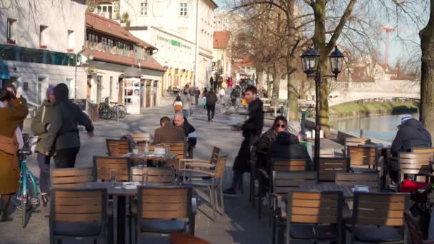 Ljubljana, Slovenya. Mart 2022 'de şehir merkezindeki Ljubljanica nehri kıyısındaki açık kafelerde insanlar görüldü.. — Stok video