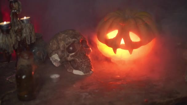 Halloween. Strašidelná halloweenská dýně s vyřezávanou tváří na stole v tmavé místnosti s lidskou lebkou a zvířecí lebkou — Stock video