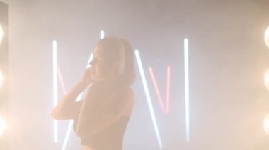 Arka planda sis dumanında dans eden sanatçı genç kadın kulaklıkları. Kendine güvenen zarif beyaz kadın dansçı modern performansı bale hareketleri ile prova ediyor.