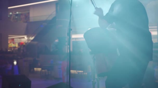 Чоловік грає на етнічних барабанах, стоячи на сцені в димі і прожекторах — стокове відео