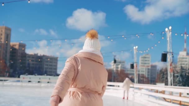Fiatal mosolygós nő korcsolyázás kívül jégpálya központi tér karácsonykor, aktív téli szabadidő a meleg napsütéses napon. Kézzel fogható. Amatőr kaukázusi női jégkorcsolyázó — Stock videók