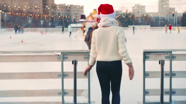 Joven mujer sonriente Santa sombrero patinaje sobre hielo fuera en pista de hielo vestido suéter blanco. Vacaciones de Navidad, ocio activo de invierno Efecto de mano. Amateur caucásico hembra patinador de hielo — Vídeos de Stock