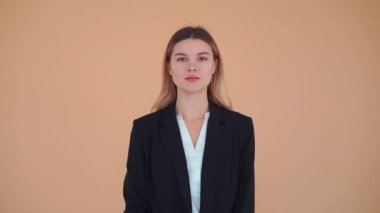 Genç bir iş kadını, siyah ceketli beyaz gömlekli, kollarını göğsüne kavuşturmuş. Stüdyoda, soluk renkli arka planda tek başına duruyor.