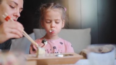 Çocuk restoranda saşimi yiyor. Annesiyle birlikte suşi ve sashimi yiyen küçük bir kızı evin içinde vur. Beyaz kadın çocuk Japon mutfağını tadıyor. 