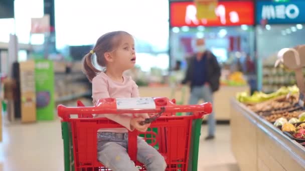 Kind, kleines Mädchen 5 Jahre sitzt Einkaufswagen im Supermarkt, während Mutter Waren auswählen, um sie zu kaufen Weibliche Kind Einkaufswagen Lebensmittelgeschäft oder Supermarkt. Kleines Kind beim Einkaufen. — Stockvideo