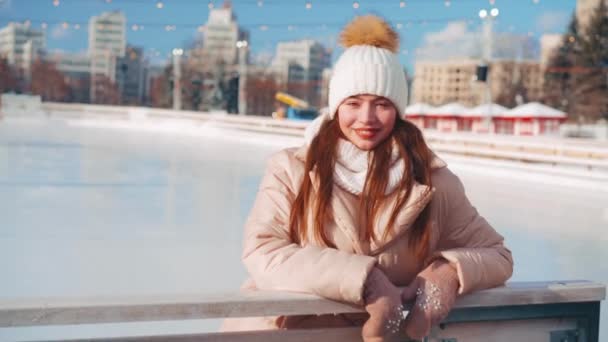 Joven mujer sonriente patinaje sobre hielo fuera en pista de hielo plaza central de la ciudad en las vacaciones de Navidad, ocio activo de invierno en un día cálido y soleado. Efecto de mano. Amateur caucásico hembra patinador de hielo — Vídeos de Stock