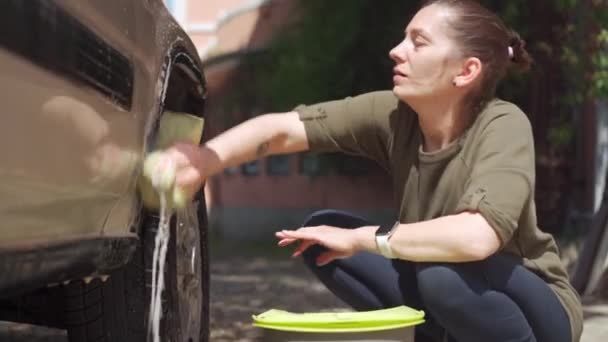Vrouw wast auto met shampoo en washandje in haar tuin in de buurt van huis. Blanke vrouw wassen auto met spons in de buurt van huis — Stockvideo