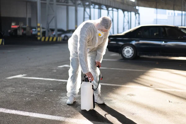 Beyaz elbiseli bir adam karantina sırasında yüzey antibakteriyel dezenfektan püskürtücü sıkarak ekipmanları hazırlıyor pompayı pompaya pompalıyor.