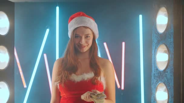 Karácsonyi Ünnepi eladás koncepció Nő öltözött Mikulás kalap dob pénzt, miközben álló megvilágított neon háttér — Stock videók