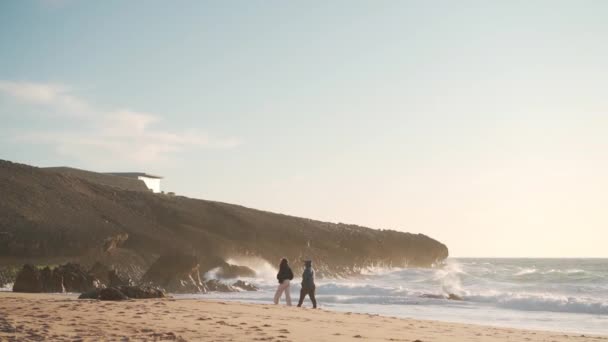 Dwie dorosłe kobieta spacery ocean plaża na wiosnę w zachód słońca światło ekstremalne długo strzelać nierozpoznawalne kobieta tylny widok spacery morze brzeg — Wideo stockowe