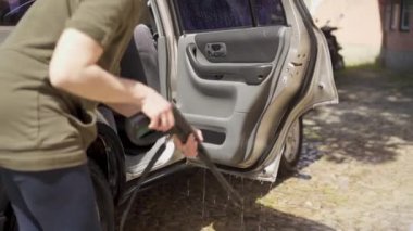 Kadın evinin yakınındaki avlusunda şampuan ve bez ile araba yıkıyor. Beyaz kadın yüksek basınçlı su teçhizatı pompasıyla araba yıkıyor.