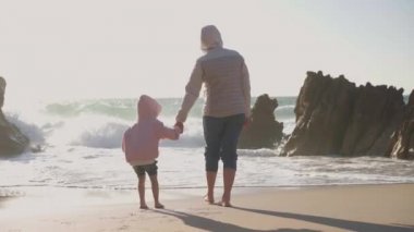 Anne ve çocuk baharda okyanus kumsalında oynuyorlar, çıplak ayakla çıplak ayakla video efekti giyiyorlar.