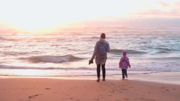 Matka i dziecko bawią się w ocean wiosną, ubierają ciepłe ubrania boso ręczny efekt wideo — Wideo stockowe