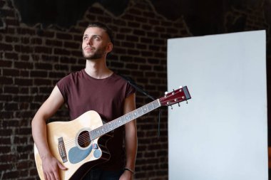 Akustik gitarlı bir adam beyaz tahta müzik okulu konseptinin yanında duruyor. Beyaz tenli erkek gitarist kapalı mekanda yazı tahtası ile.