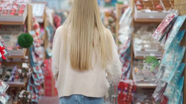 クリスマス・ショッピング。冬の市場でクリスマスオーナメントのリアビューを見てショッピングカートで歩く女性はその後、笑顔のジェスチャーを好転させる私に従う. — ストック動画
