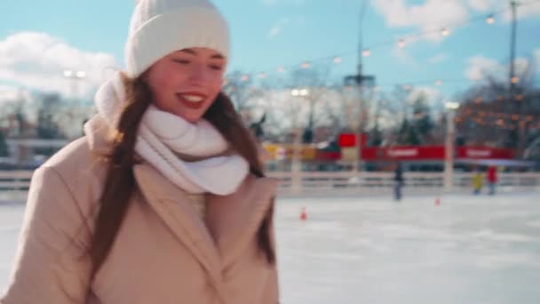 Joven mujer sonriente patinaje sobre hielo fuera en pista de hielo plaza central de la ciudad en las vacaciones de Navidad, ocio activo de invierno en un día cálido y soleado. Efecto de mano. Amateur caucásico hembra patinador de hielo — Vídeos de Stock