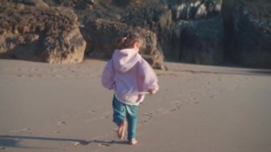 Okyanus sahillerinde koşan küçük bir çocuk. Küçük beyaz kız kumsalda koşuyor. 