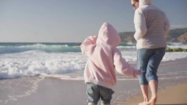 Anne olmak için koşan çocuk baharda okyanus kumsalında oynamaya çalışıyor, çıplak ayakla çıplak ayakla video efekti giyiyor.