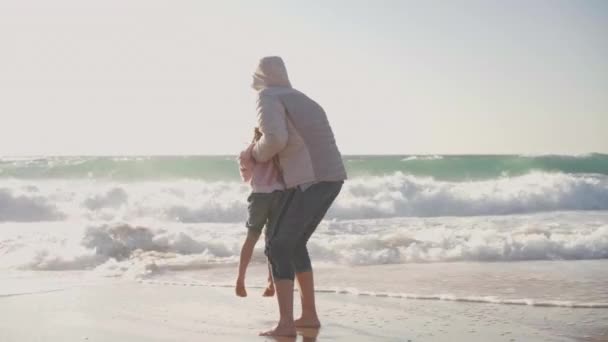 Mother and child playing ocean beach at spring, dressed warm clothes barefoot handheld video effect — Stockvideo