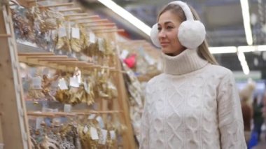Noel alışverişi. Beyaz kazak ve kürk kulaklıklar takmış, Noel süsü seçen Kafkas kadın süpermarketi. Yetişkin Kadın 30 yıldır Noel süsü alıyor.