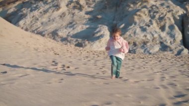 Okyanus sahillerinde koşan küçük bir çocuk. Küçük beyaz kız kumsalda koşuyor. 