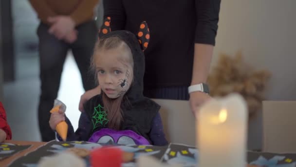 Klein meisje versieren glazuur handgemaakte Halloween koekjes gekleed Halloween carnaval kostuum met hoorns — Stockvideo