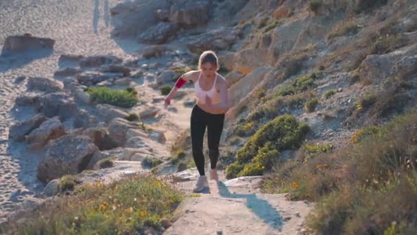Idrottskvinna springer på stranden sten trappor väg slow motion. Bedårande ung vuxen kaukasisk kvinna jogga utomhus vid havet njuta av hälsosam livsstil — Stockvideo