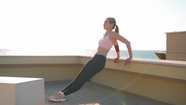 Ung vuxen passform kvinna gör triceps dips övningar under utomhus cross training träning. Fitness kvinnlig modell träning sommardag nära havet stranden. — Stockvideo