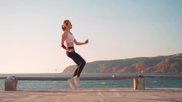 Athletic kvinna träning hoppa motion träning. Sportig kaukasisk kvinnlig hoppning konditionsträning med hav och berg landskap bakgrund. En hälsosam livsstil. — Stockvideo