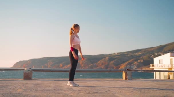 Lento movimento tiro jovem atleta do sexo feminino praticando exercícios corporais inferiores. Ela fazendo frente movendo-se lunge contra cenário incrível montanha oceano. — Vídeo de Stock