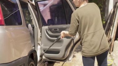 Kadın evinin yakınındaki avlusunda şampuan ve bez ile araba yıkıyor. Beyaz kadın yüksek basınçlı su teçhizatıyla araba yıkıyor.