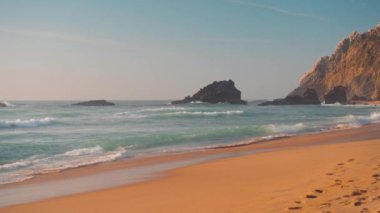 Okyanus vahşi kumsal fırtınalı havası. Praia da Adraga kumlu plajı manzaralı arka plan, Sintra Cascais, Portekiz el bilgisayarı etkisi. Mavi enerjinin ve berrak okyanus suyunun canlılığı