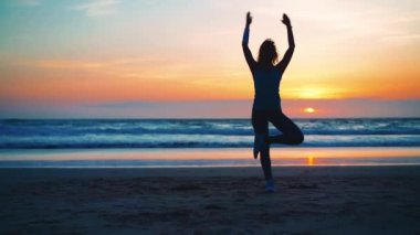 Siluet Kadın yoga ağacı alıştırması yaz tatili plaj mutluluğu ve rahatlığı ile meditasyona poz veriyor. Yogayla sakin kadın egzersizleri okyanus sahilinde altın günbatımında meditasyon yapar. Ruh Sağlığı. 