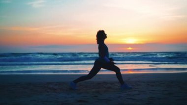 Siluet Kadın yoga savaşçısı pozu yaz tatili kumsalında mutluluk ve rahatlama ile meditasyon yapıyor. Yoga yapan sakin kadın egzersizleri, gün batımlı okyanus sahillerinde meditasyon yapar. Ruh Sağlığı. 