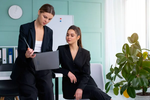 Young women leaders are checking financial statements from paper documents. Two female confident business worker dressed black suit in office checking financial document looking folder and discussing